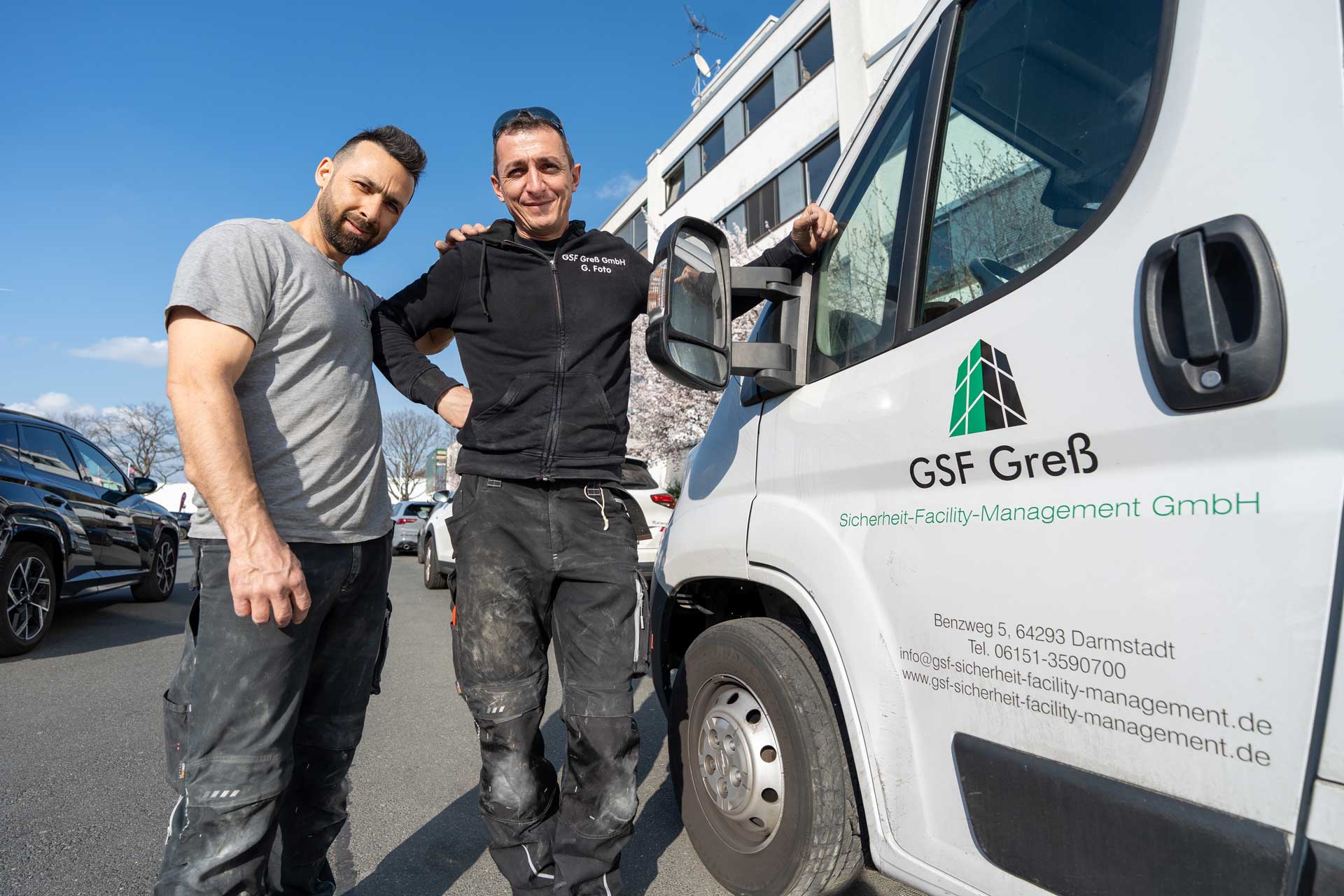 Zwei Handwerker mit freundlichen Gesichtern stehen neben einem weißen Firmenwagen