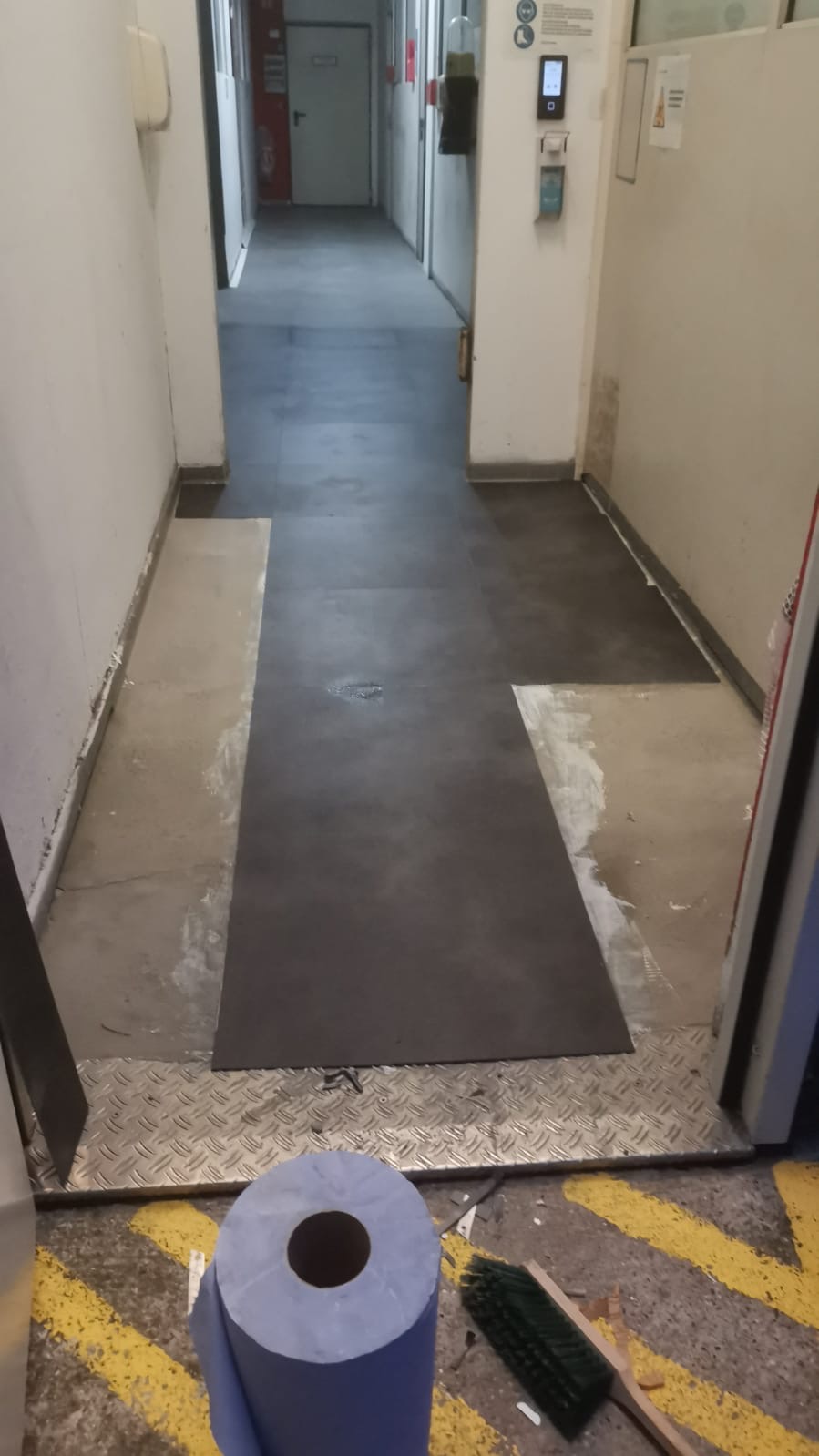 Ein Flur mit frischem grauem Bodenbelag, daneben Reinigungsutensilien und blaue Rolle