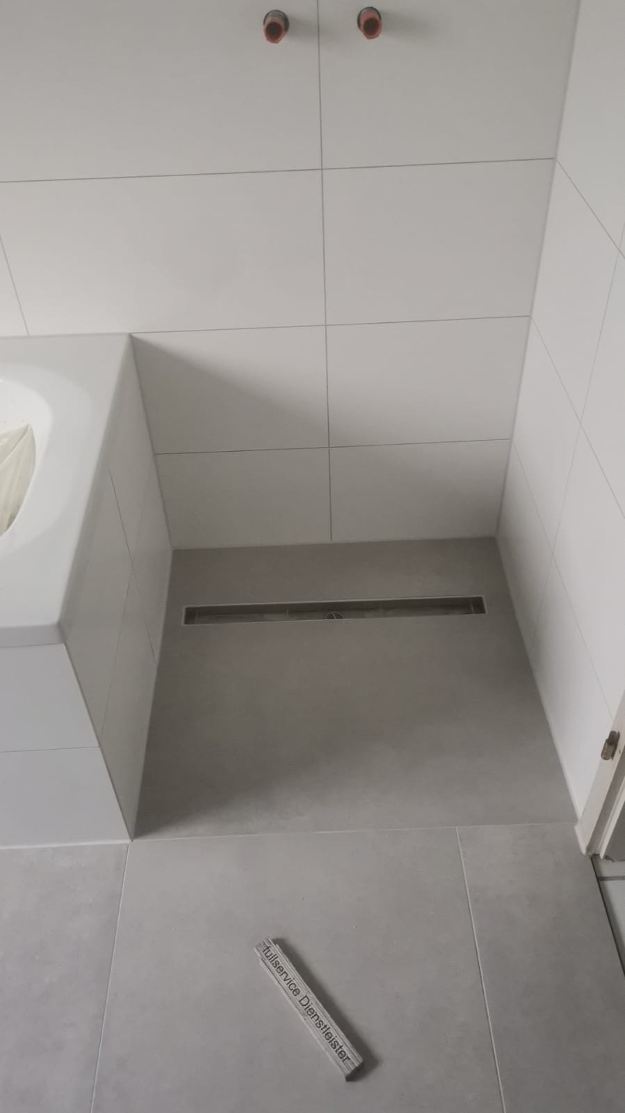 Ein grauer gefliester Duschbereich mit Wandablauf und zwei roten Wasseranschlüssen