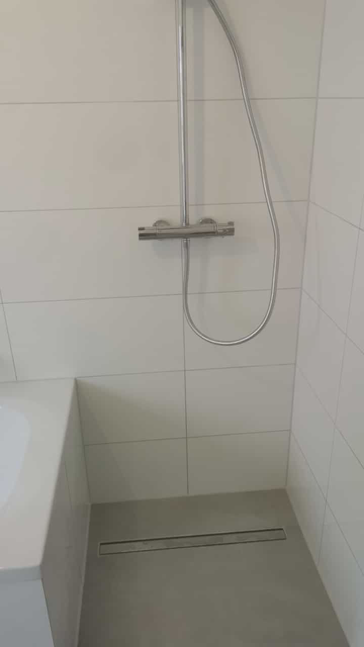 Eine moderne Dusche mit silberner Armatur vor weißen Fliesen und Bodenablauf