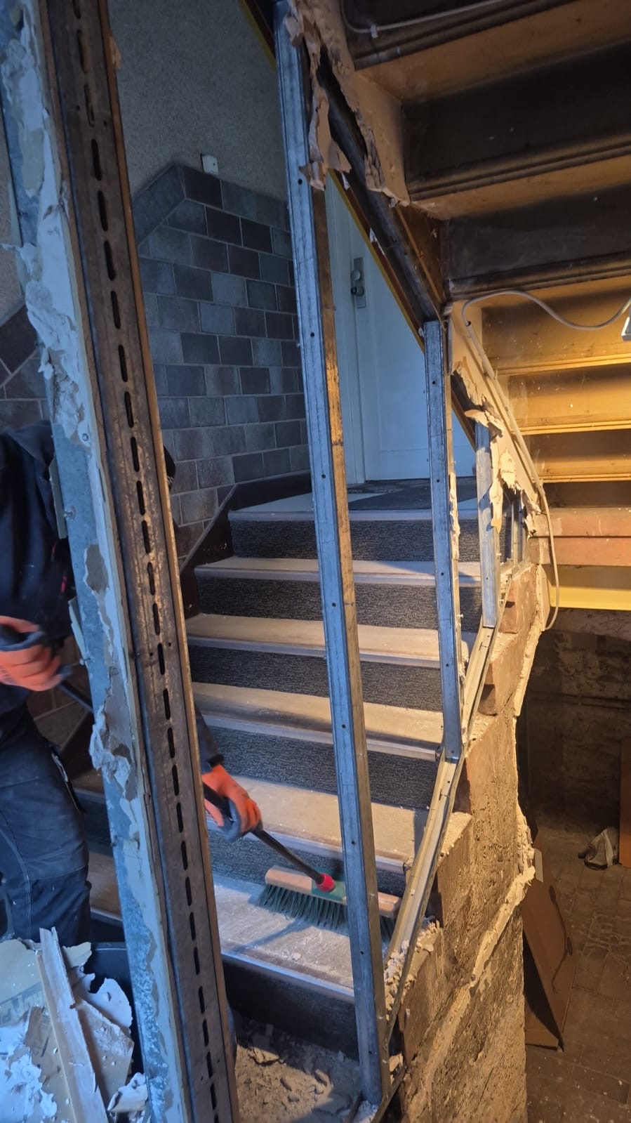 Eine Person im dunklen Arbeitsoutfit entfernt Bauschutt vor einer grauen Treppe