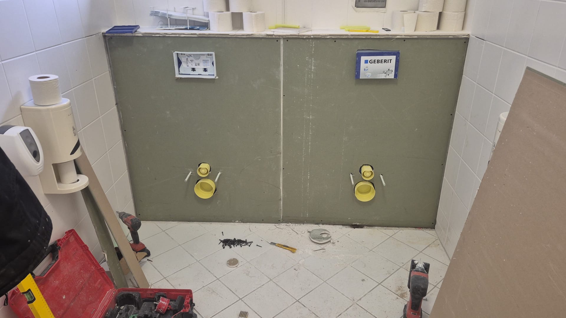 Zwei Toiletteninstallationen mit gelben Anschlüssen auf grauer Wand in hellem Bad