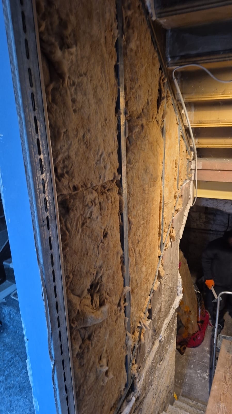 Eine Wand mit gelber Dämmwolle und offenen Metallprofilen unter einer Treppe