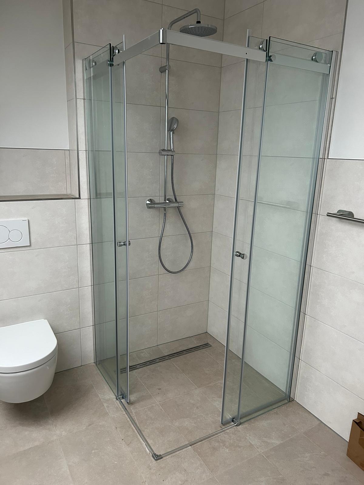 Moderne Dusche mit Glaswänden und silberner Duscharmatur in einem hellen Bad