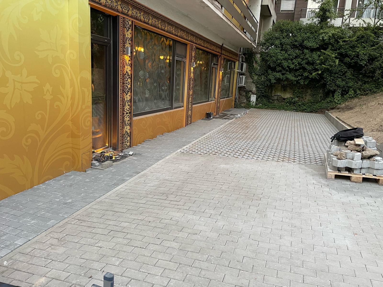 Ein modern gepflasterter Hof vor einem gelb verzierten Gebäude mit großen Fenstern
