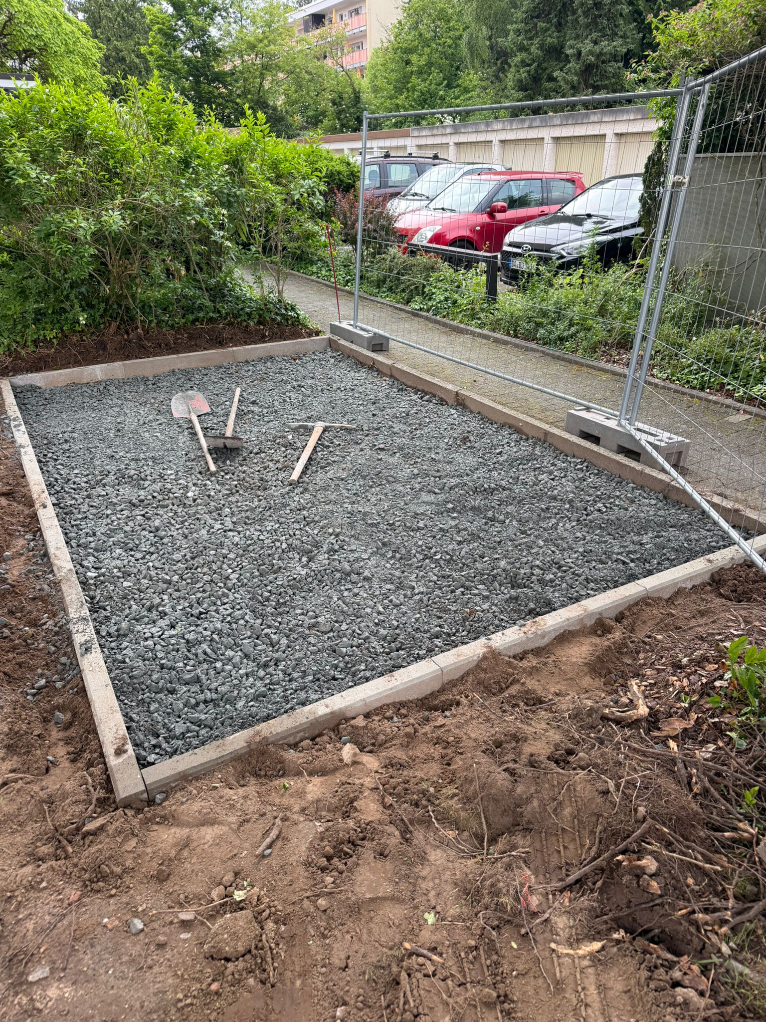Eine Baustelle mit Schotterfläche, Werkzeugen und grüner Bepflanzung im Hintergrund