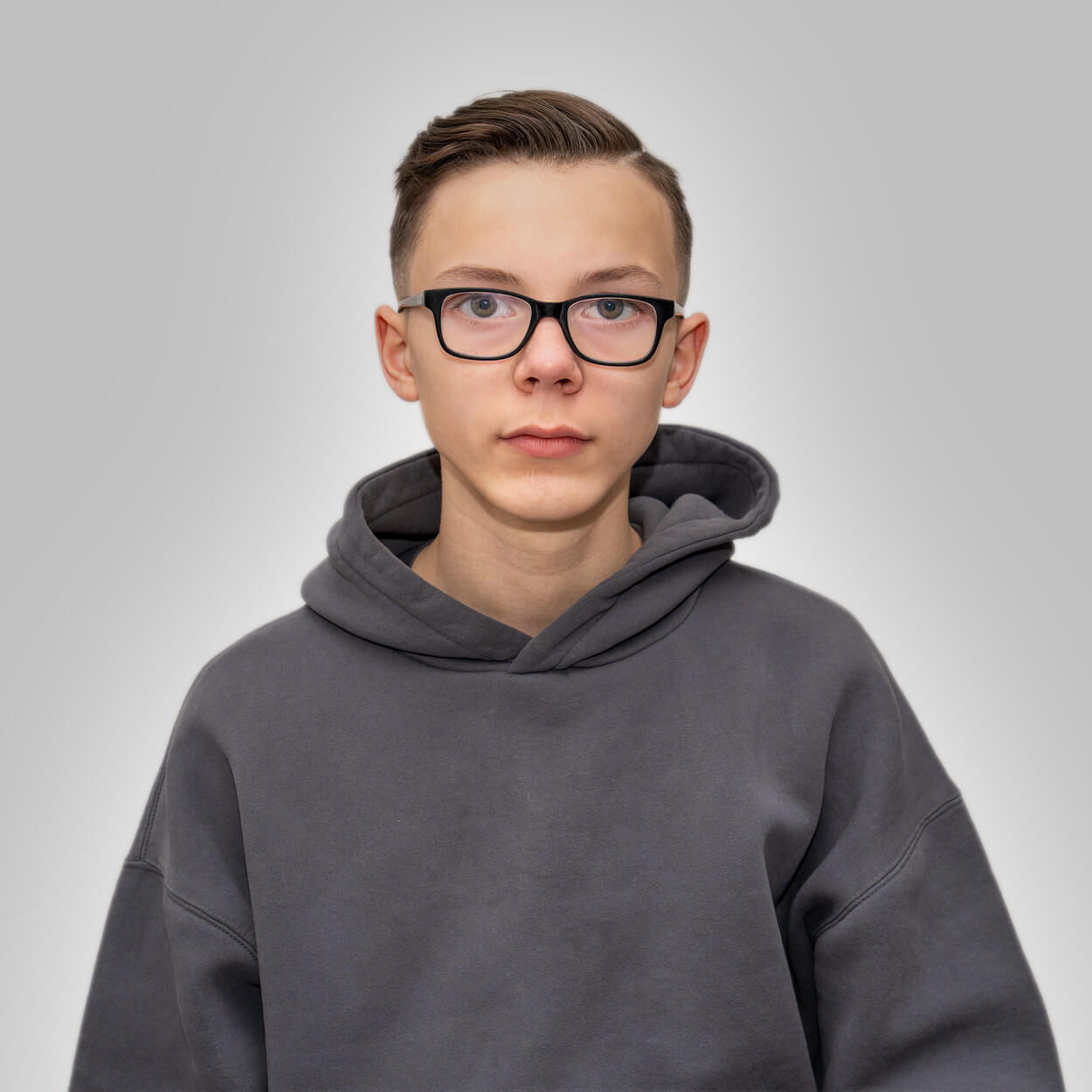 Ein junger Mann mit Brille und grauem Hoodie blickt ruhig in die Kamera