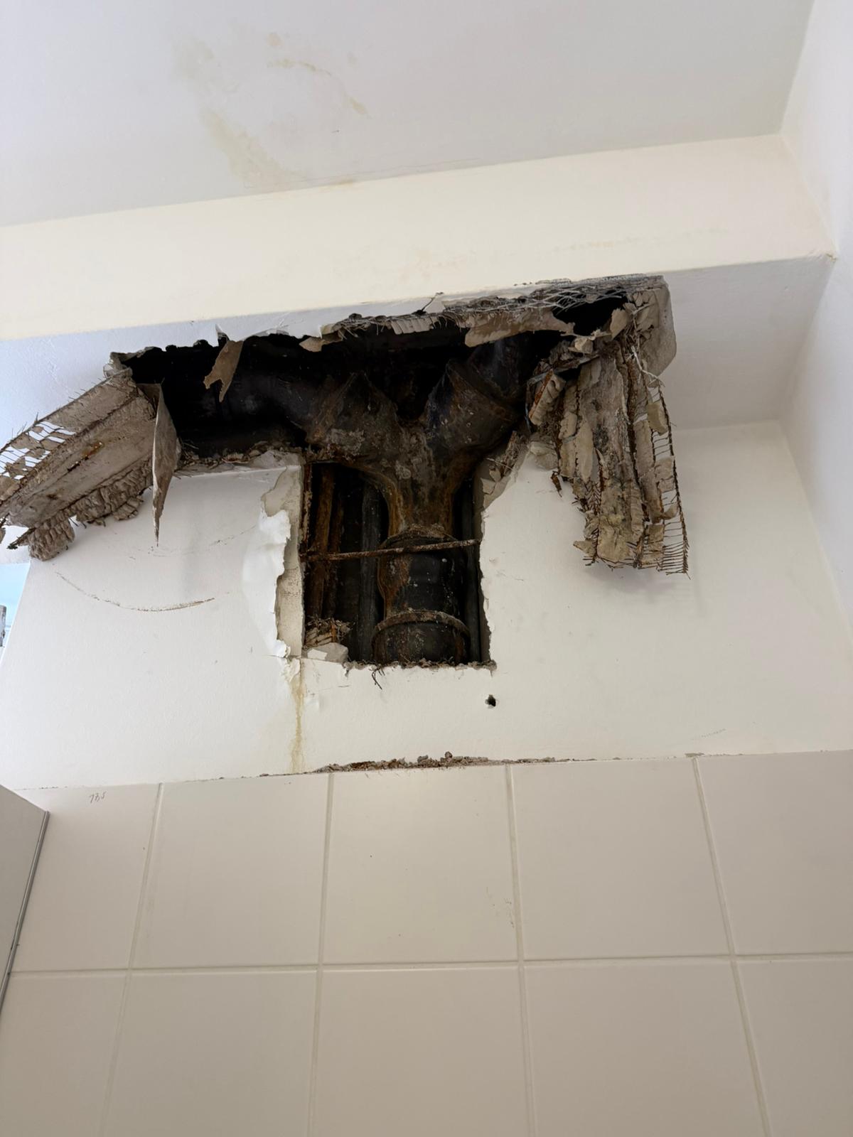 Großes Loch in weißer Wand mit sichtbarem alten Rohr und abblätterndem Putz