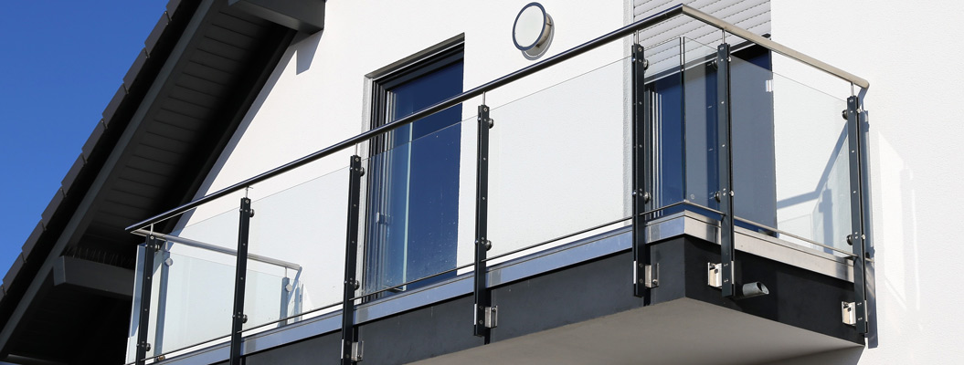 Moderner Balkon mit Glasgeländer und Metallrahmen an weißer Hausfassade im Sonnenschein