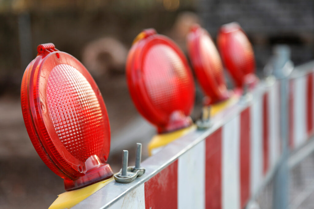 Mehrere rote Warnleuchten leuchten auf einer Baustellenabsperrung aus Metall