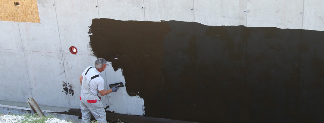 Ein älterer Mann streicht konzentriert mit schwarzer Farbe eine Betonwand