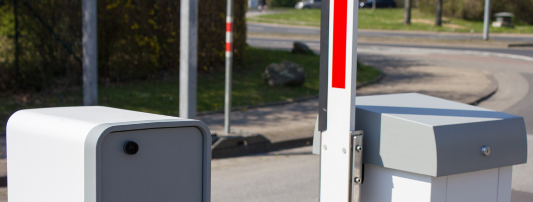 Schranke mit weißem und rotem Balken an einer sonnigen Straße und heller Steuerbox
