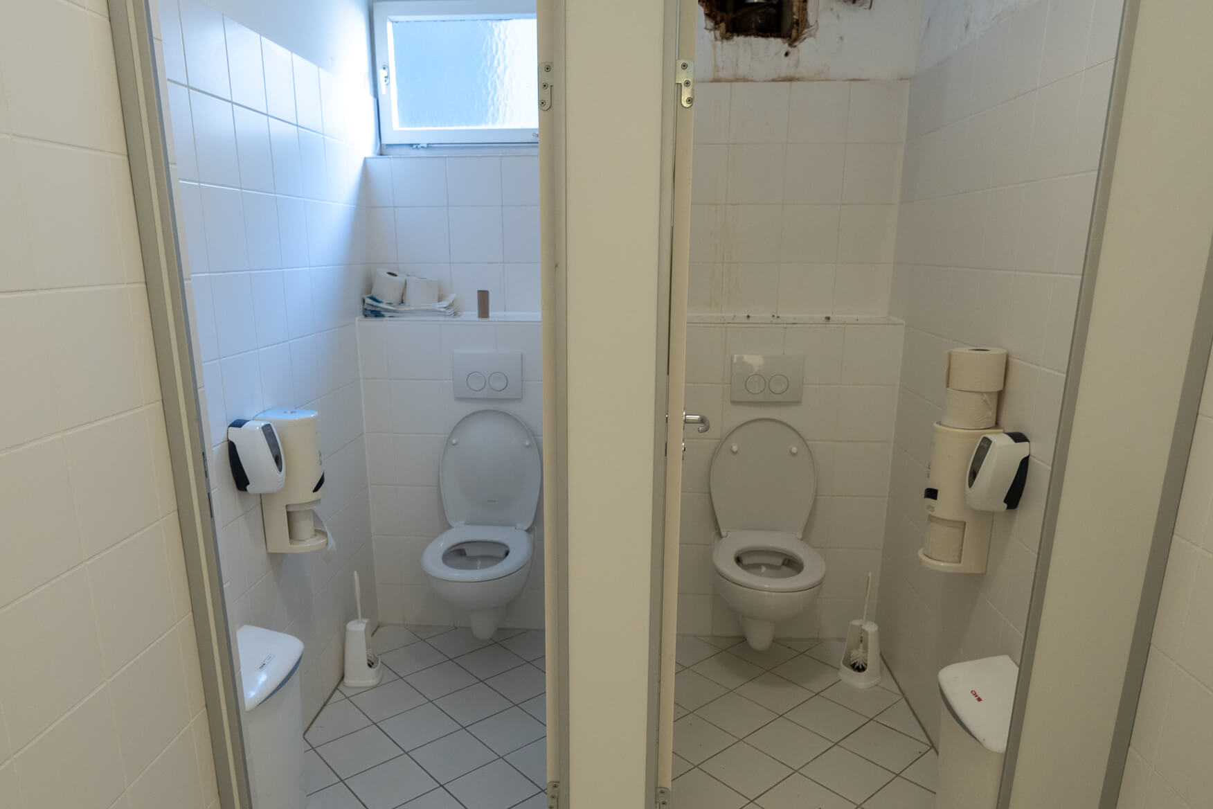 Zwei nebeneinanderliegende Toiletten mit weißer Keramik und Papierrollen im Sanitärraum