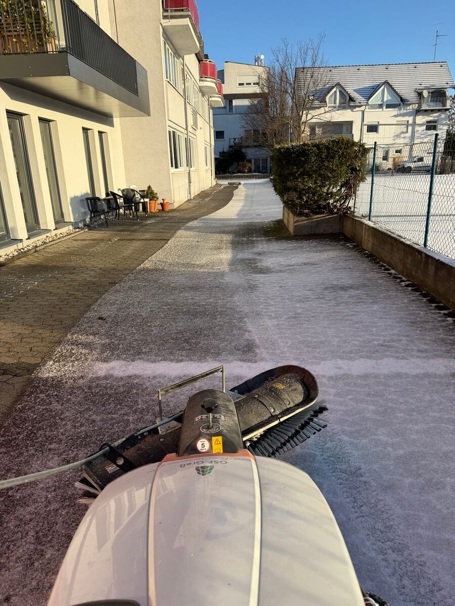 Ein schneebedeckter Gehweg wird mit einer Kehrmaschine bei Sonnenschein geräumt