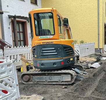Ein gelber Hyundai Bagger steht auf einer Baustelle mit weißen Absperrungen und Erde