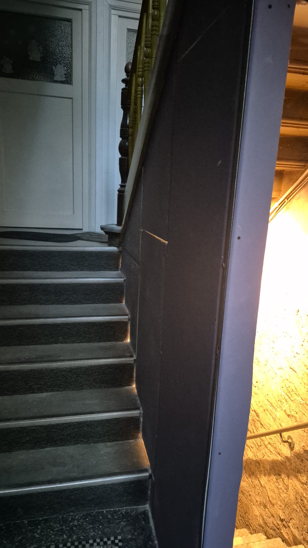 Ein Treppenaufgang mit grauen Stufen neben einer gelb beleuchteten Wand im Flur