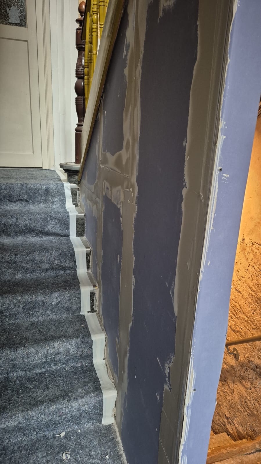 Eine renovierte Treppenwand mit frischem Putz neben grauem Teppich und Holzgeländer