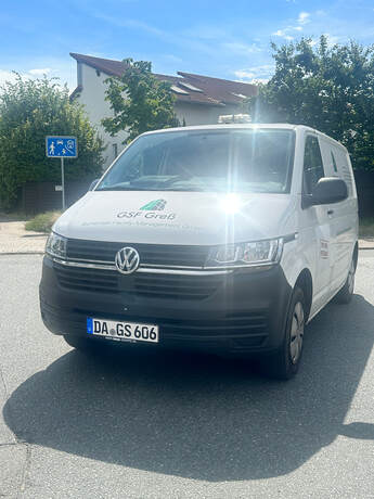Weißer Volkswagen Transporter mit grünem Logo und glänzender Motorhaube im Sonnenlicht