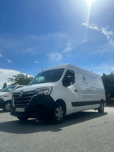 Ein weißer Lieferwagen mit Firmenlogo steht bei Sonnenschein auf einem Parkplatz