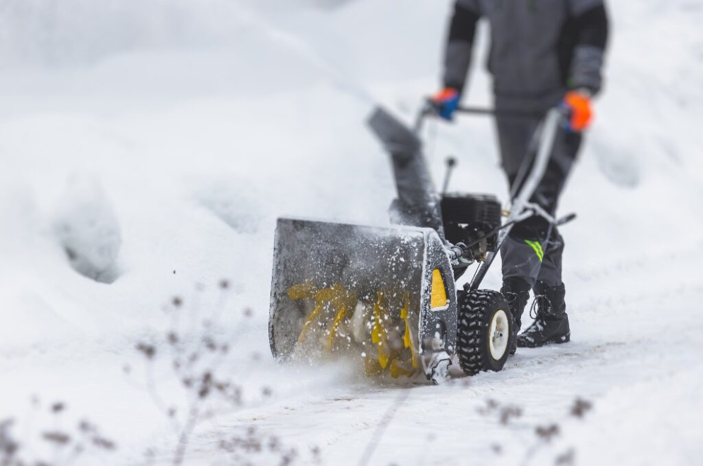 Process of removing snow with portable blower machine, worker dressed in overall workwear with gas snow blower removal on the street during winter