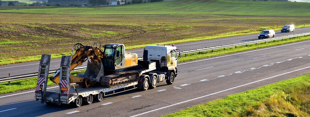 Trailer truck with long platform transport the Excavator on highway. Earth mover backhoe on heavy duty flatbed vehicle for transported. Long Haul and Shipping Services. Loading on Low Bed Trailer