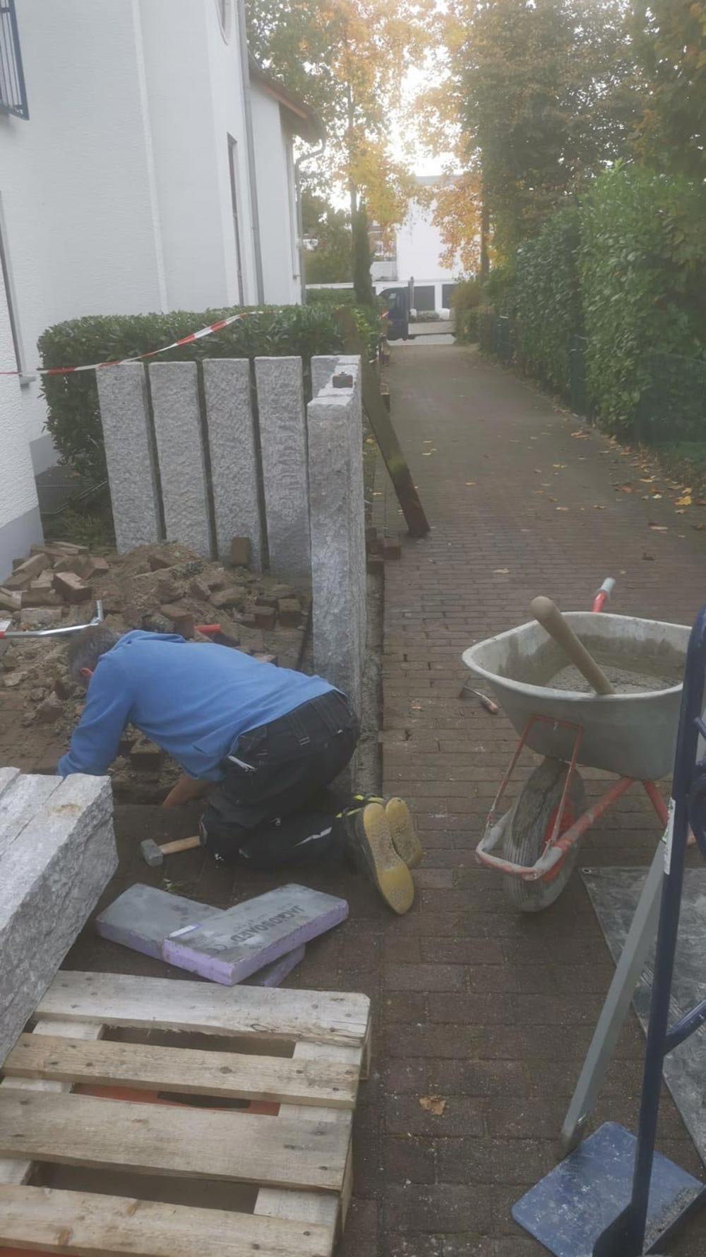Bauarbeiter kniet konzentriert neben grauen Steinen und Schubkarre