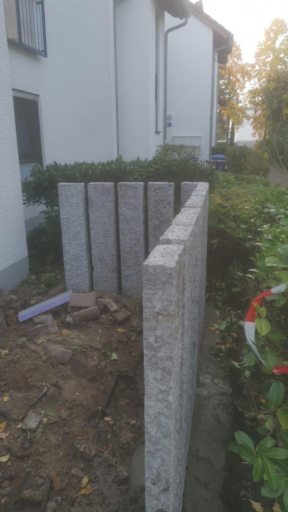 Graue Granitplatten als kleine Mauer neben weißem Haus im Garten bei Herbstlaub