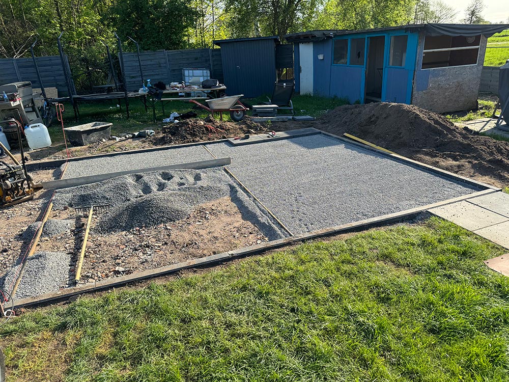 Baustelle mit grauen Betonplatten und blauem Schuppen im Gruenen