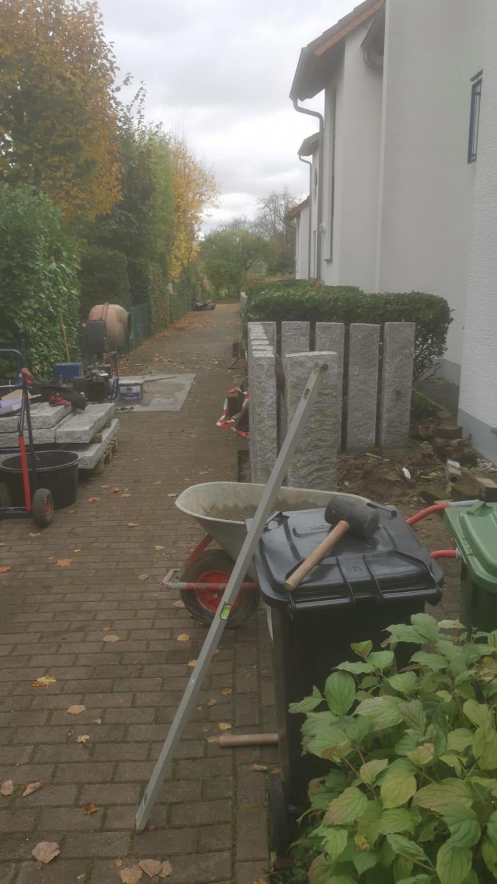 Herbstlicher Gartenweg neben Haus mit Baustelle, Schubkarre und Werkzeug