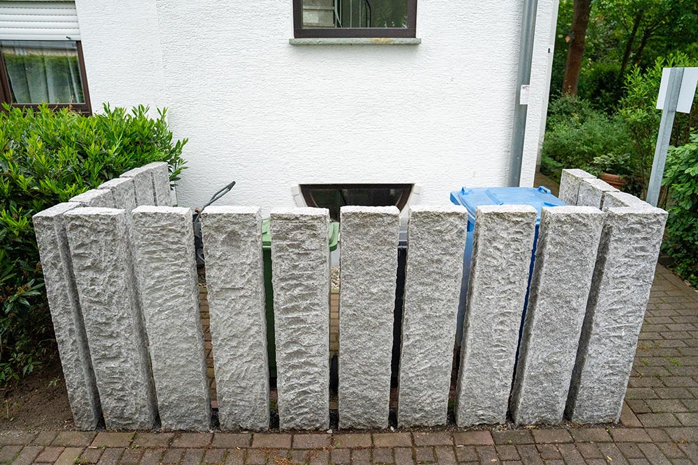 Graue raue Betonpfeiler stehen ordentlich vor weißer Hauswand mit blauem Band