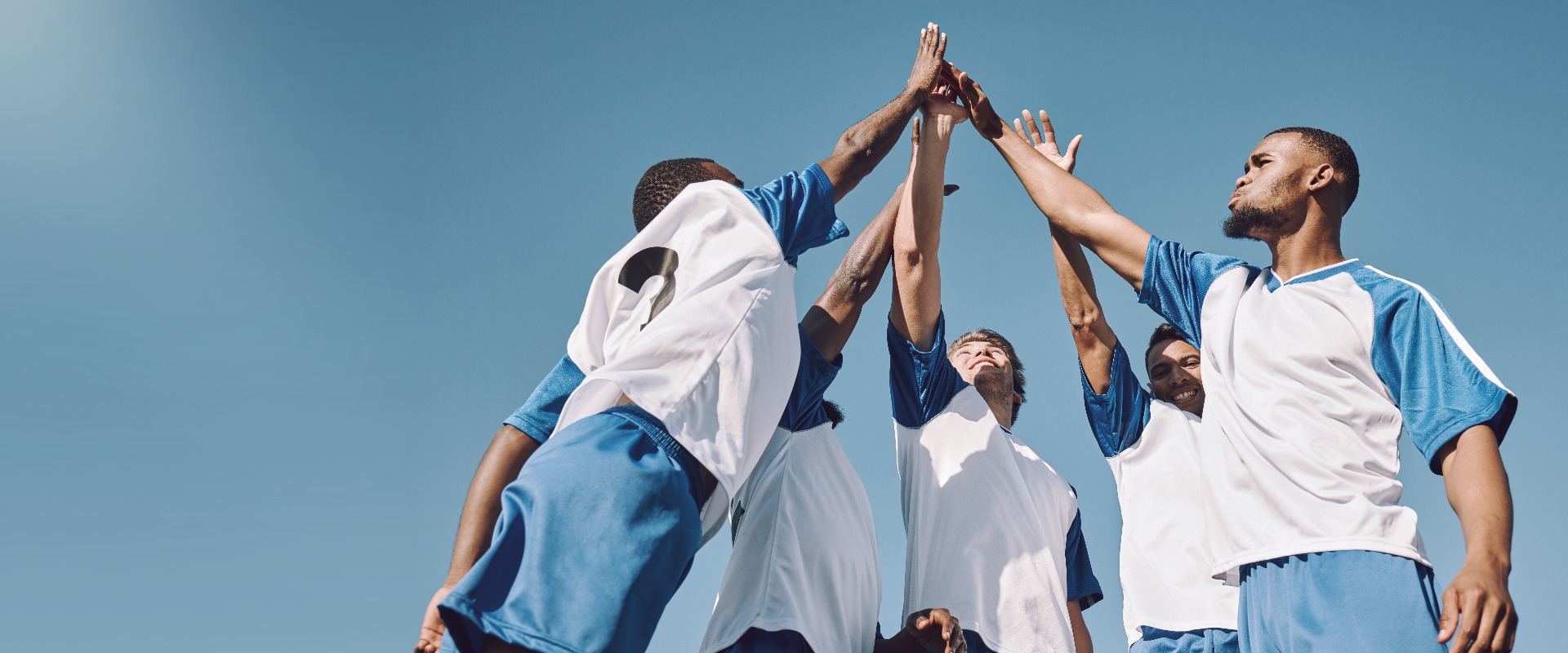 Fußball, High-Five im Team und Männer, die bei einem Sportwettbewerb oder Spiel ihren Sieg feiern – dank Teamwork auf dem Platz. Eine Football-Meistermannschaft, die motiviert die Hände zum Ziel, zur Leistung und zu sportlichen Erfolgen reckt